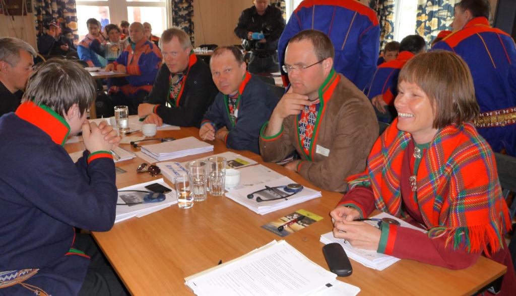 Personar kledde i samisk drakter rundt eit bord. Foto.