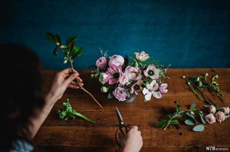 Nærbilde av to hender som jobber med å sette sammen en blomsteroppsats. Foto.