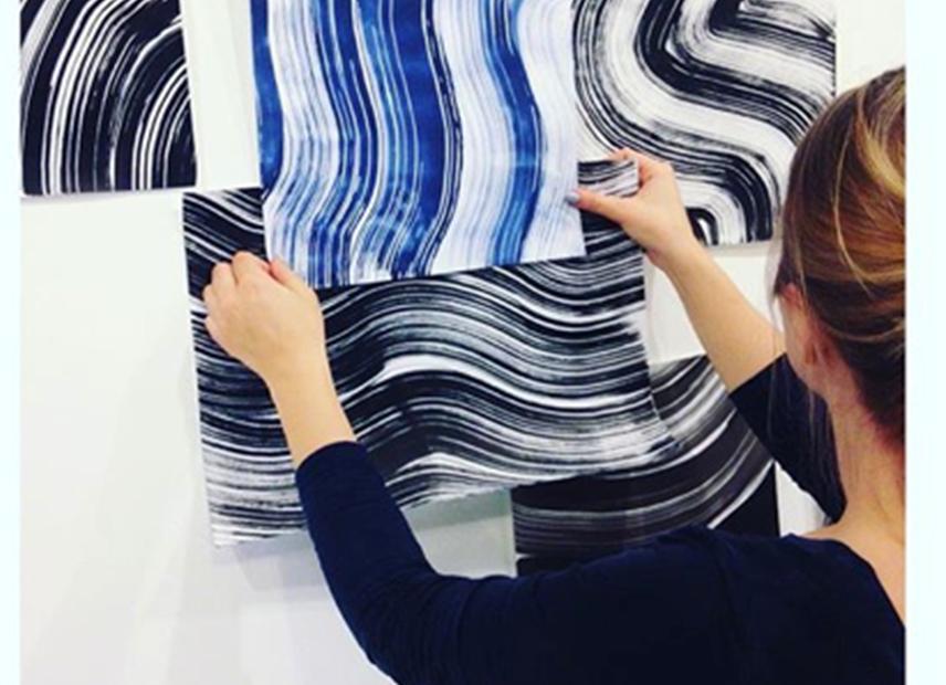 Designar vurderer ulike tekstiltrykk med svinga linjer i blått, kvitt og svart. Ho held dei opp mot veggen. Foto.
