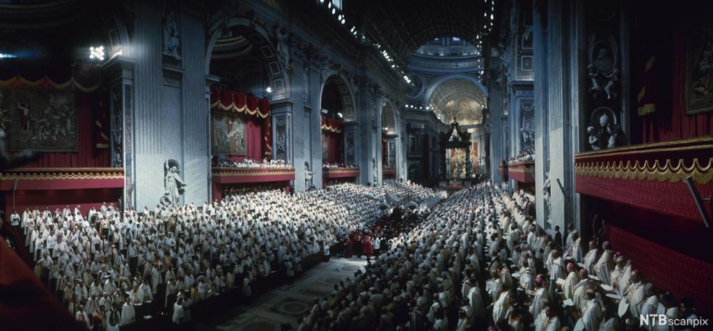 Mange mennesker kledd i hvitt samlet i stort kirkerom. Foto.