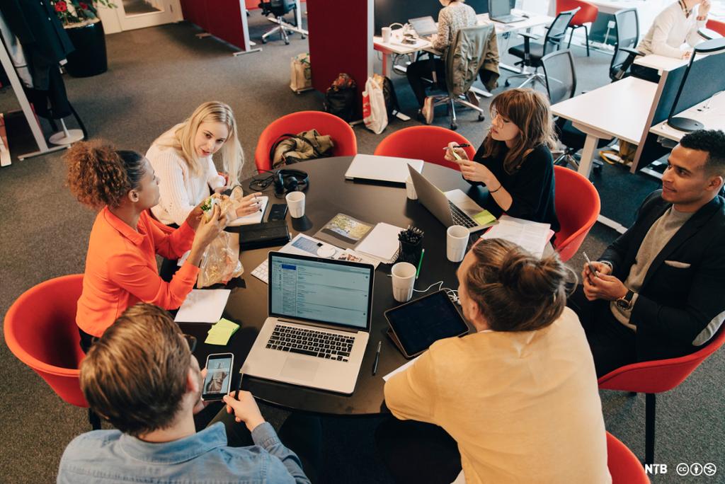 Seks personar sit rundt eit møtebord i eit kontorlandskap og diskuterer. Foto.