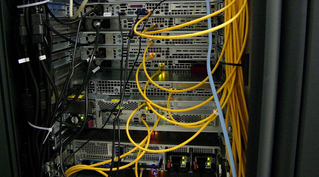 Baksiden av en server-rack. Flere servere er stablet oppå hverandre, de har strøm og nettverkskabel tilkoblet. Foto.