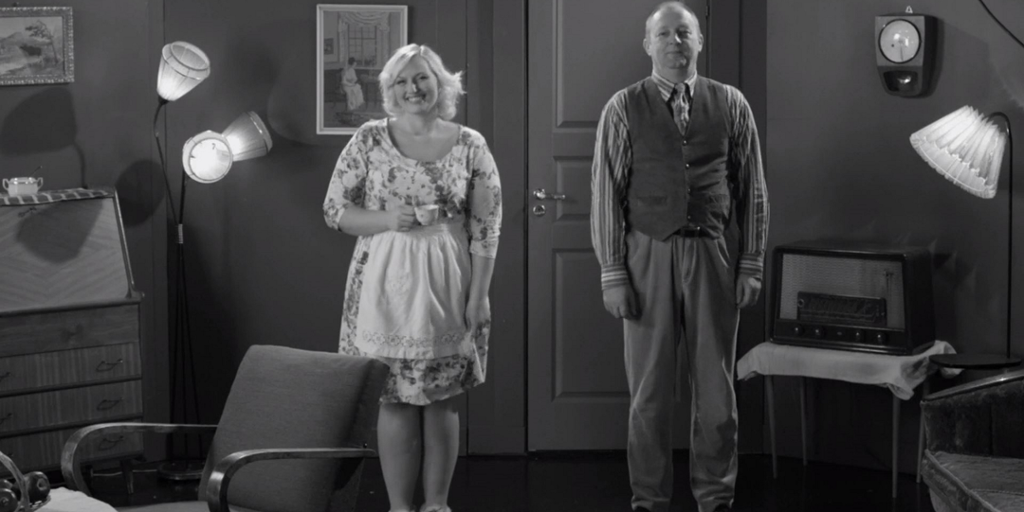 Mann og dame smiler mot kameraet. Bildet er i svart-hvitt, og klærne og dekoren er fra 1960-tallet. Foto.