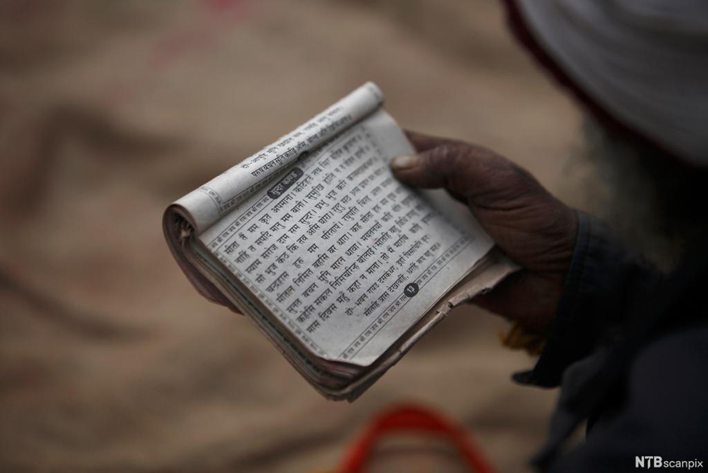 Mann holder bok med tekst på et indisk språk. Foto.
