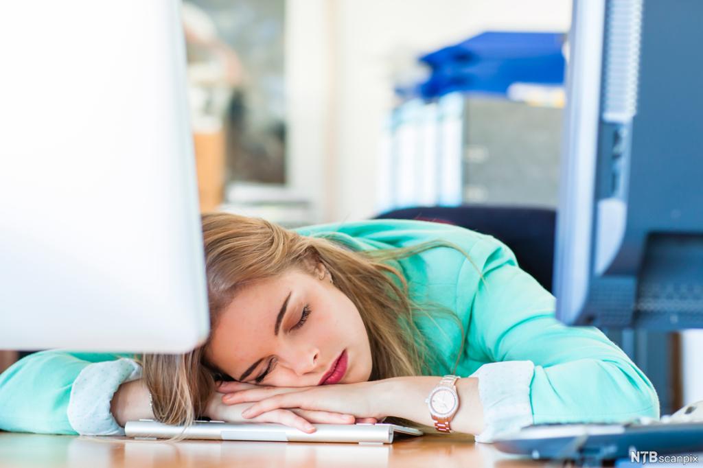 En ung kvinne sover på PC-tastatur. Foto. 