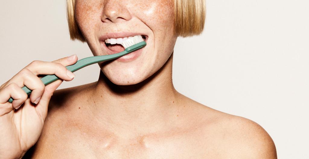 Kvinne pusser tennene med grønn tannbørste. Munnen er i fokus. Foto.