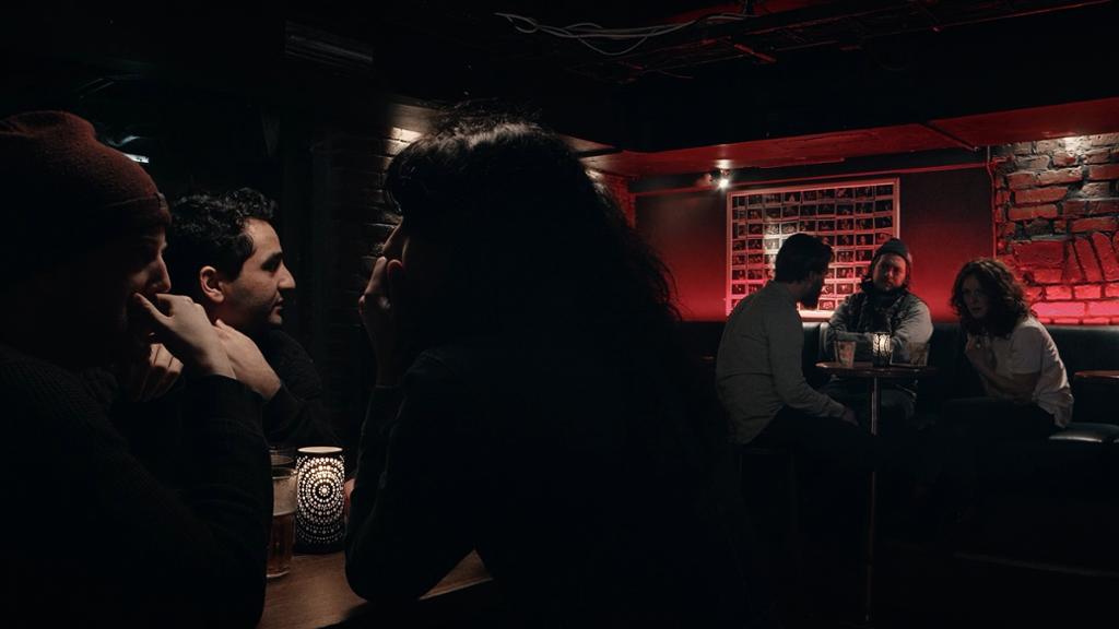 Unge kvinner og menn i små grupper i ein bar. Foto.