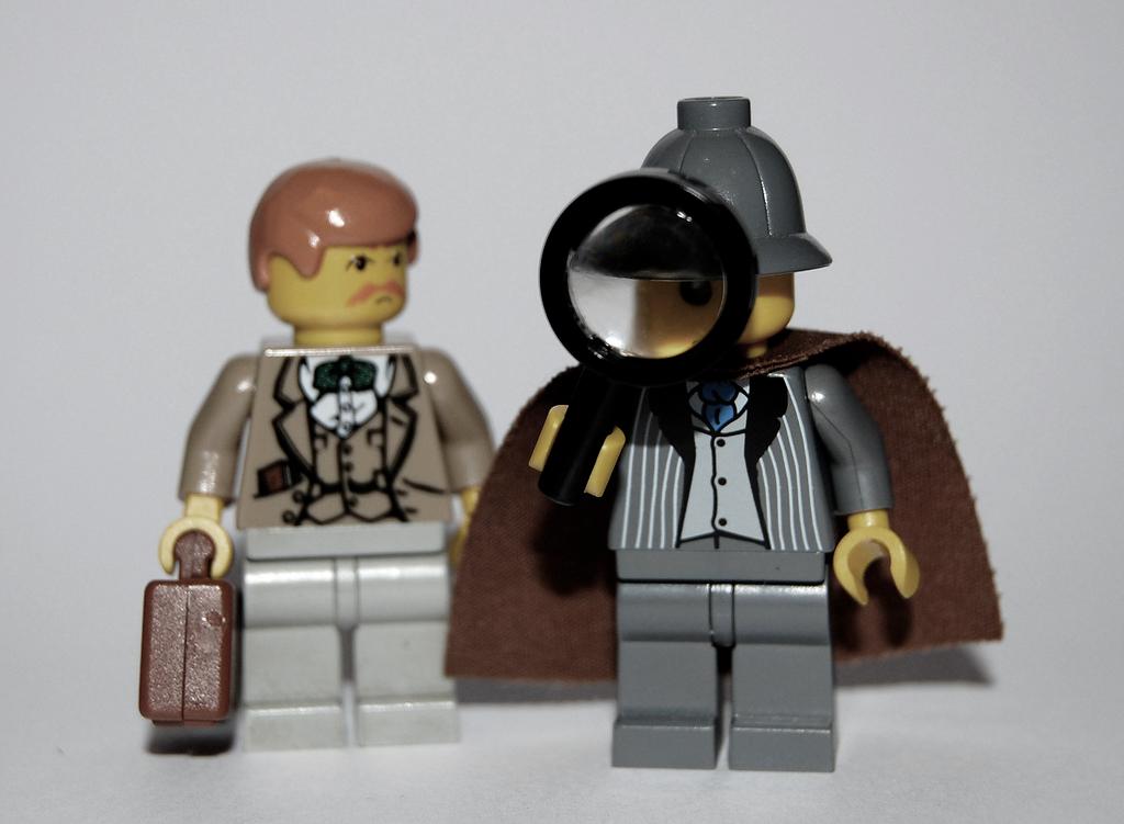 To Lego-figurar, den eine med hatt og lupe, den andre med stresskoffert. Foto.
