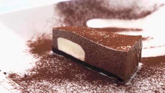 Et stykke sjokolademoussekake servert på en hvit tallerken, drysset med kakaopulver. Foto.