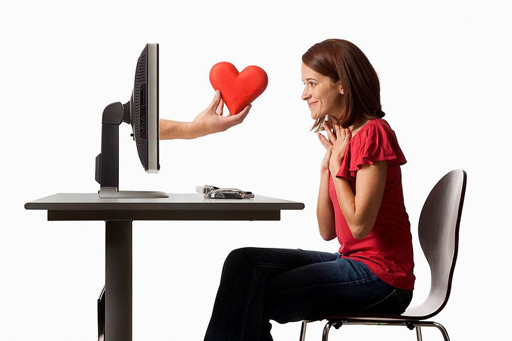 Hånd med et hjerte kommer ut av en dataskjerm foran en kvinne. Foto.