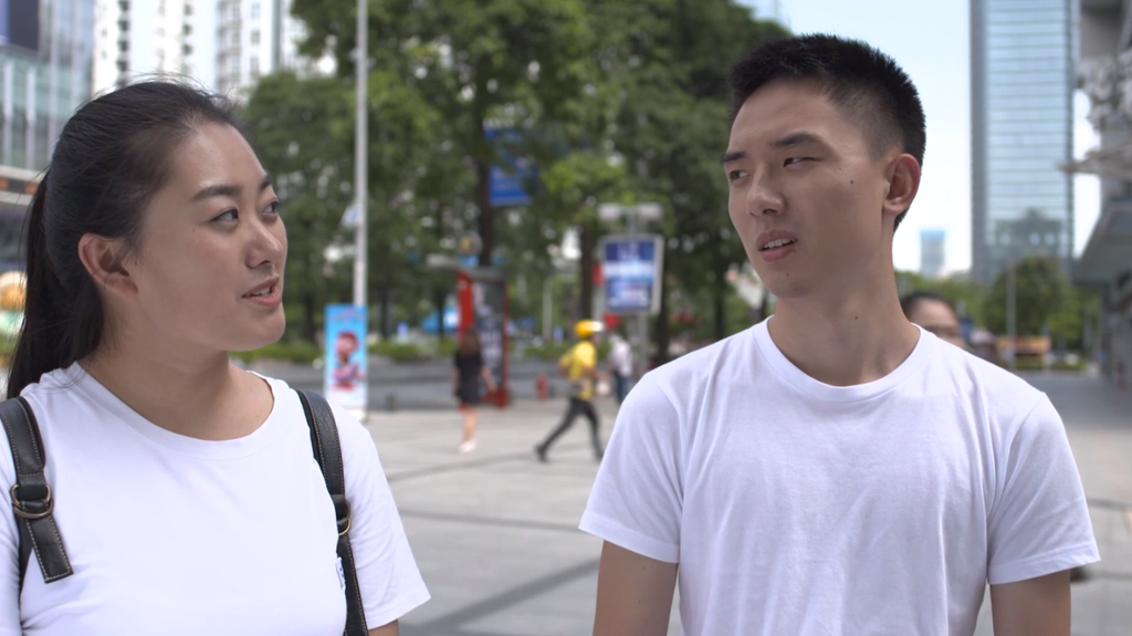 Jente og gutt i hvite t-skjorter snakker med hverandre i sentrum av en by. Foto.