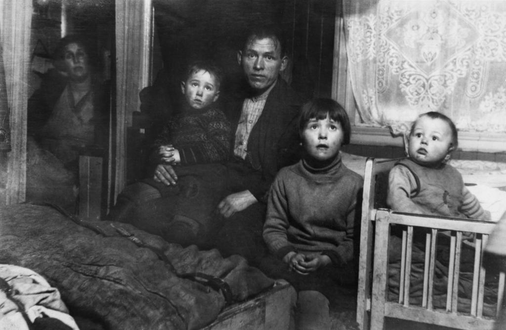 En familie på et lite soverom i en arbeiderbolig, ca 1930. Foto.