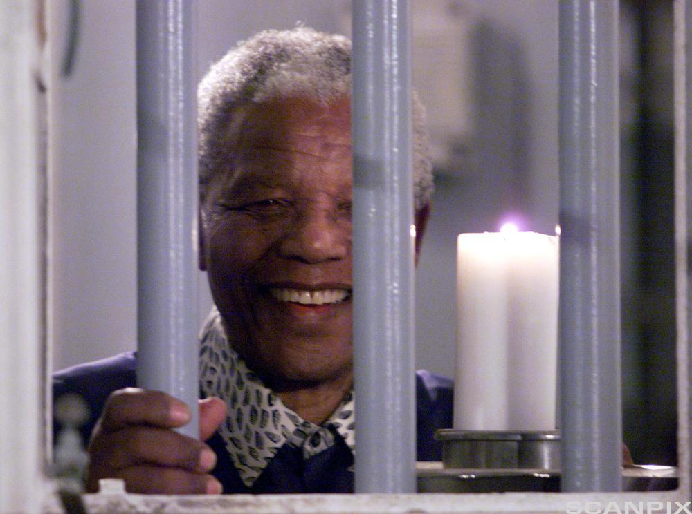 Former president Nelson Mandela holds a symbolic millennium candle through the bars of the prison cell on Robben Island