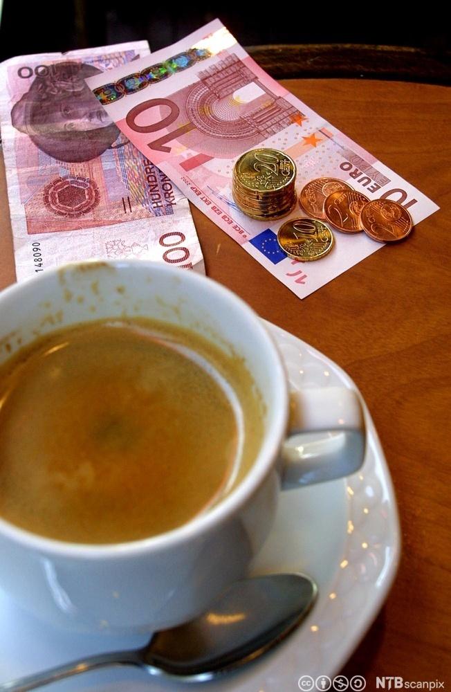 En kaffekopp på et bord med noen pengesedler ved siden. Foto.