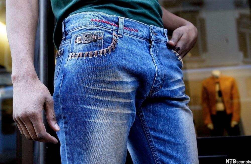 En person med slitte jeans holder en hånd i lomma. Foto.