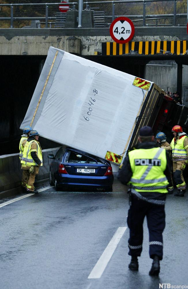 Redningsmannskap står ved ein lastebil som har velta og delvis smadra ein personbil. Foto.