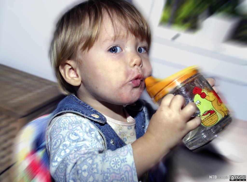 Barn drikker vann fra babykopp. Foto.