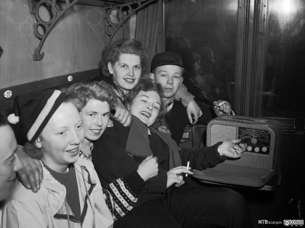 Ungdommer på vei til påskefjellet med bergenstoget i 1952 lytter til en reiseradio av typen Radionette Kurér. Foto.