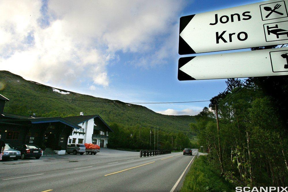 Skilt langs veien mot Tuftelia vertshus og Jons kro, vest for Geilo. Grønnkledde fjell med snøflekker i bakgrunnen. Foto.