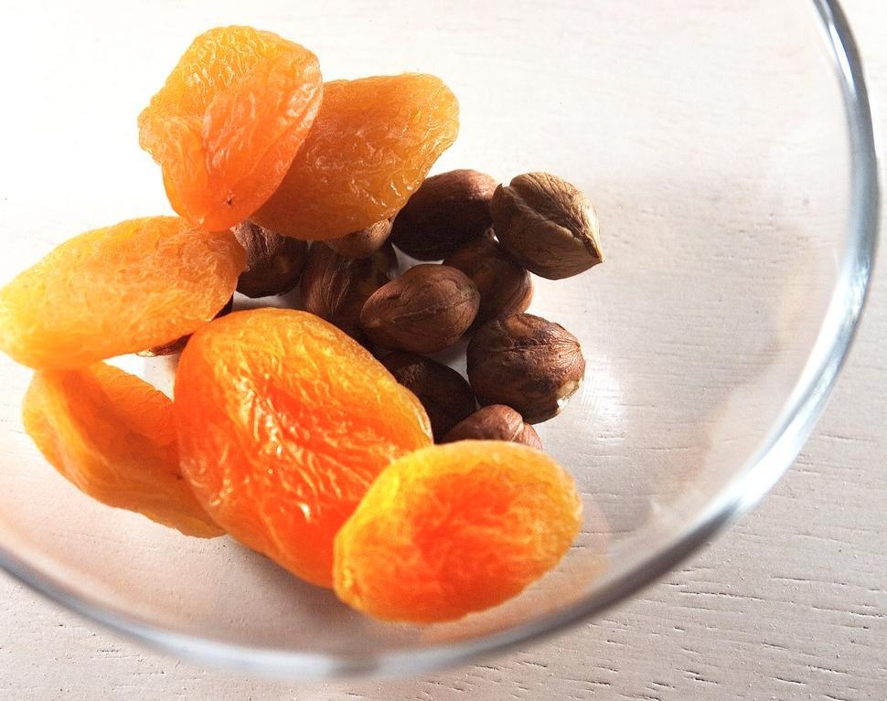 Tørkeet aprikoser som ligger litt foran noen nøtter i en blank glass skål. Foto