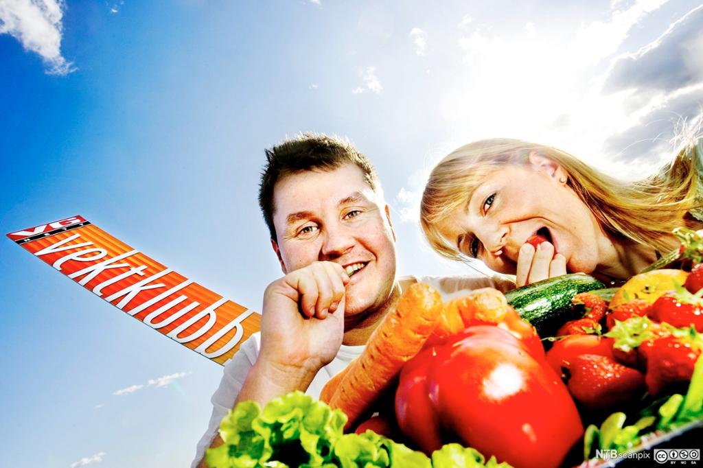 Ei dame og en mann smiler mens de forsyner seg av et bugnende grønnsaksfat. I bakgrunnen er det sol og blå himmel og et banner med logoen til VG Vektklubb. Foto.
