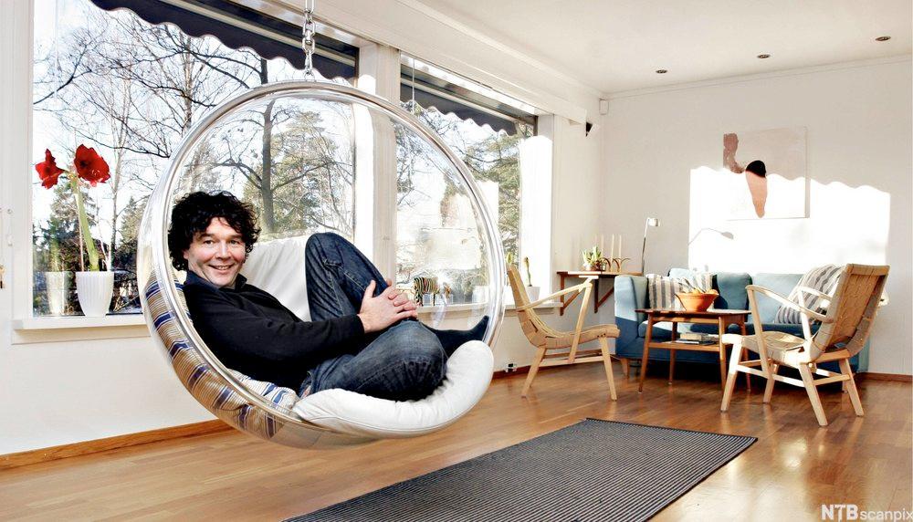 En ung mann som sitter i en designstol som henger ned fra taket. Foto.