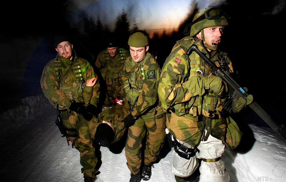 Soldater fra Telemark Bataljon redder ut "skadde" markører under en øvelse. Tre menn i kamuflasjedrakter bærer en "skadd" person mellom seg. En fjerde soldat går foran til høyre i bildet med et gevær i hendene. Foto.