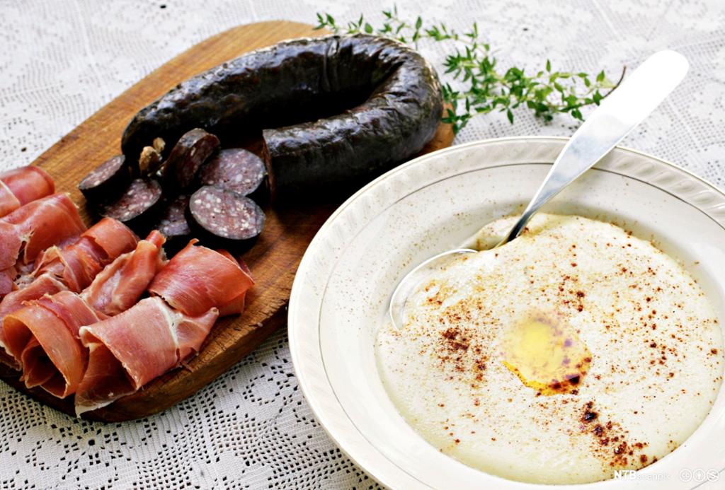 Ein skål med rømmegraut og eit fat med spekemat og frukt. foto.