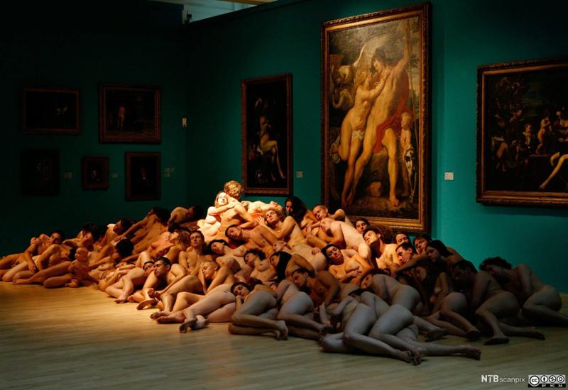 Nakne modeller ligger i haug foran malerier av nakne modeller i Museum Kunstpalast i Düsseldorf. Foto.