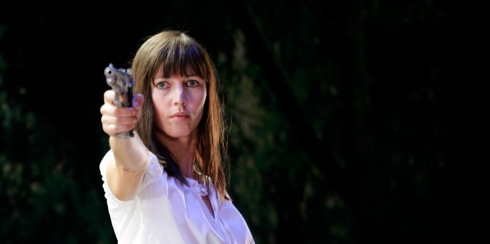 Petronella Barker som Hedda Gabler. Hun sikter med en pistol. Foto. 