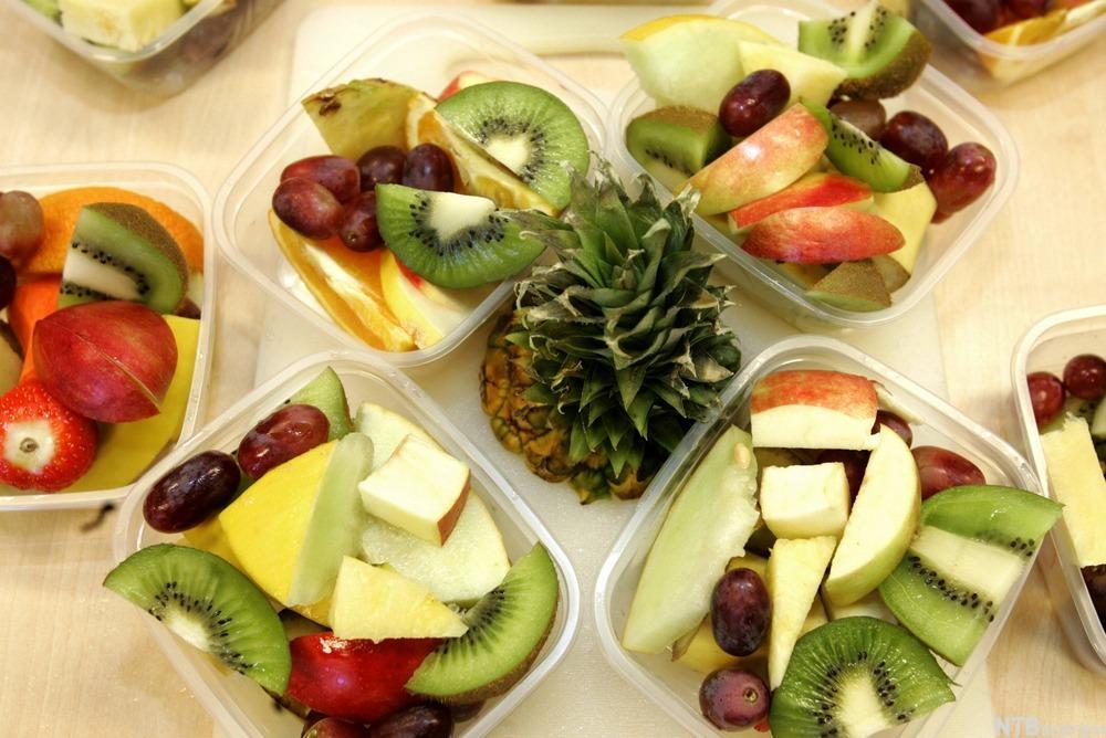 På et bord stor det plastbokser med oppskåret frukt, blant annet kiwi, melon, eple og druer. I midten er en avskåret ananastopp. Foto.