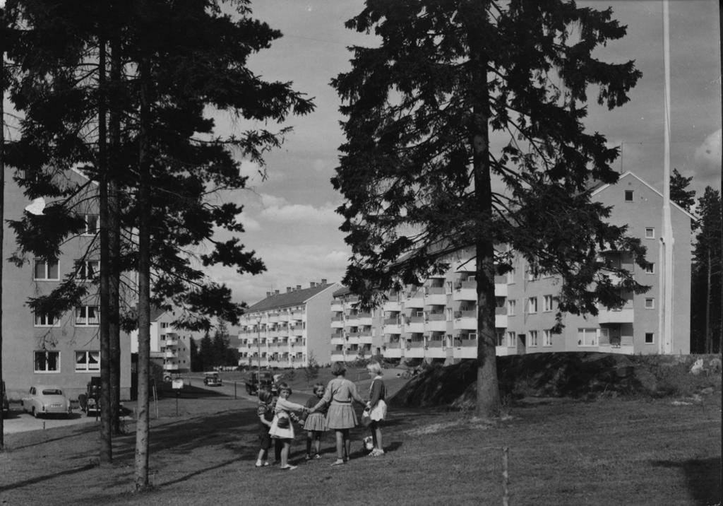 Jenter leikar på grøntområde ved bustadblokker. Svart-kvitt foto. 