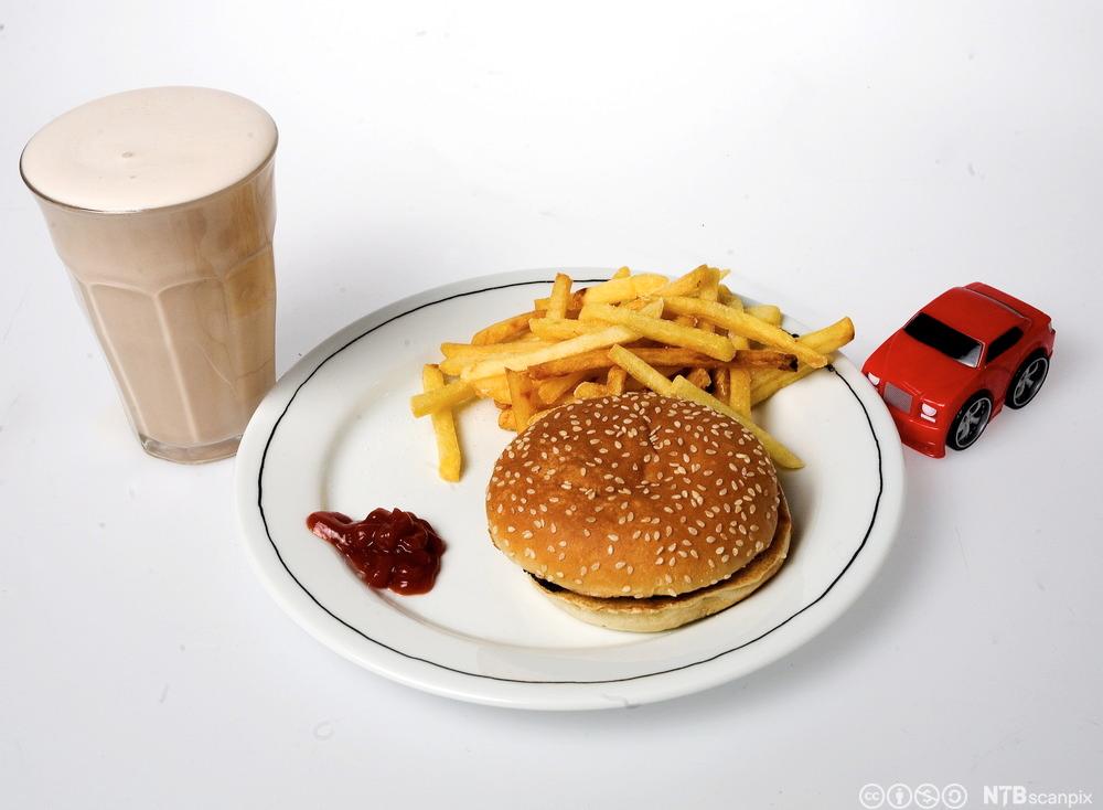 Foto av en tallerken med hamburger, pommes frites og ketsjup. Ved siden av står en sjokolademilkshake og en liten lekebil.