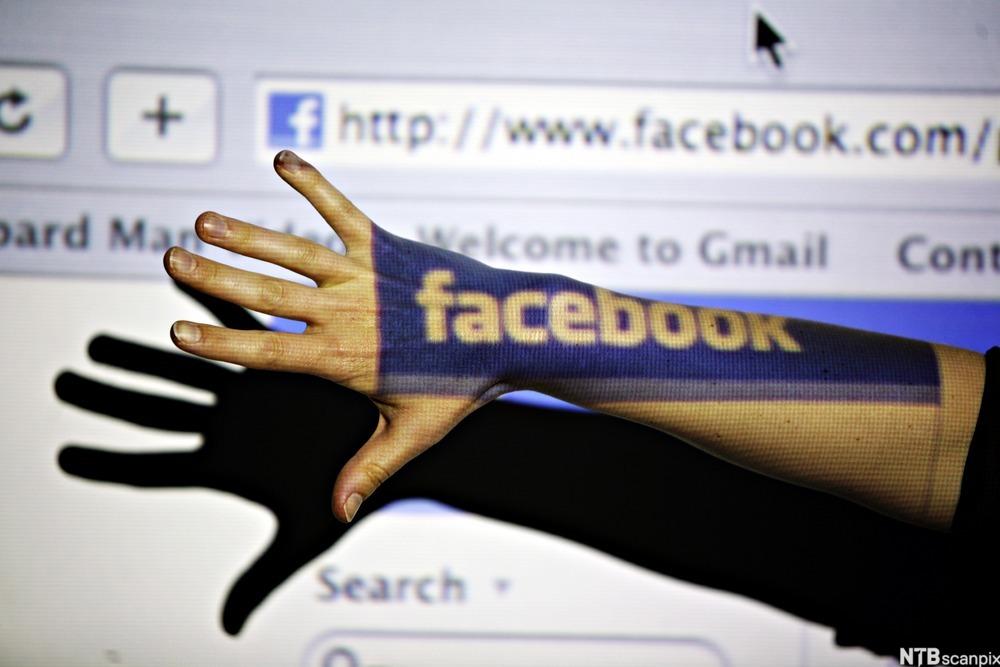 Hånd kaster skygge over en dataskjerm og får selv Facebook-logoen som en skygge på seg. Foto.