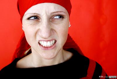 Kvinne med rødt tørkle på hodet som viser sint uttrykk. Foto.