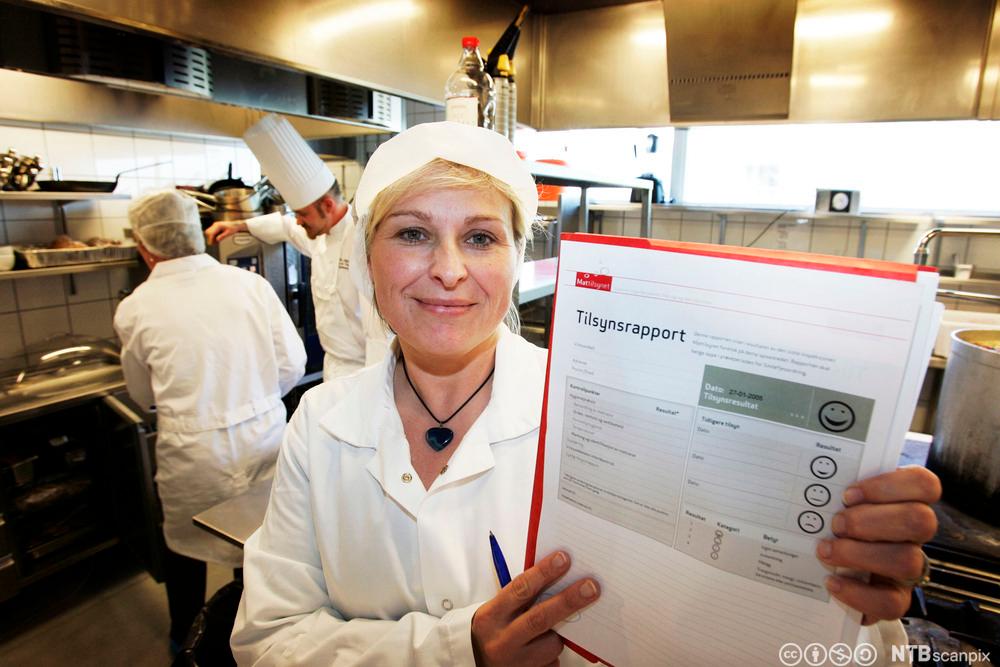 Kokk held opp ein tilsynsrapport frå mattilsynet. Foto