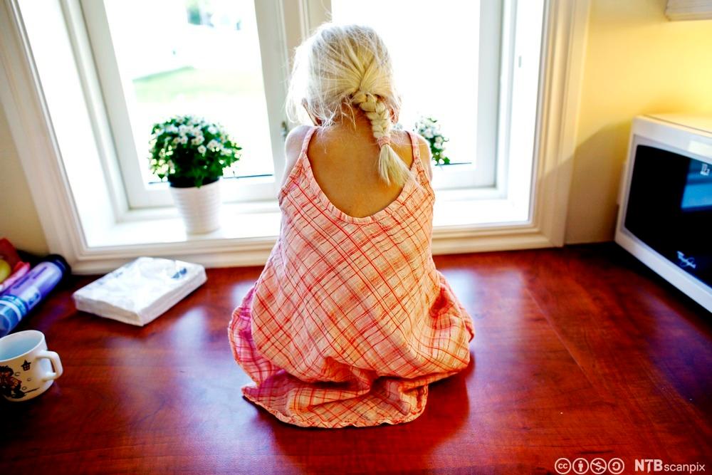 Liten jente set ut et vindu. Foto.