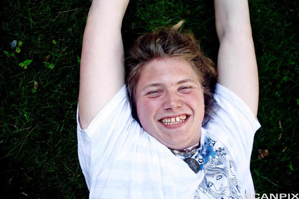 Glad, ung mann som ligger i gresset. Foto.