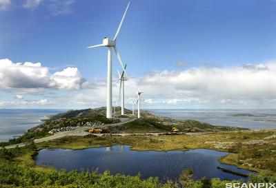 Fem vindmøller fra Hundhammerfjellet vindmøllepark står i terrenget ute ved kysten. Det er et ferskvann i forkant av vindmøllene. Foto.