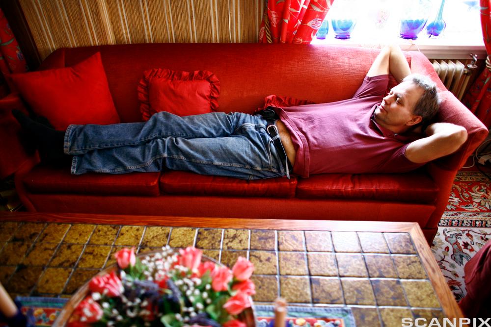 Mann som ligg på sofa og slappar av. Foto.