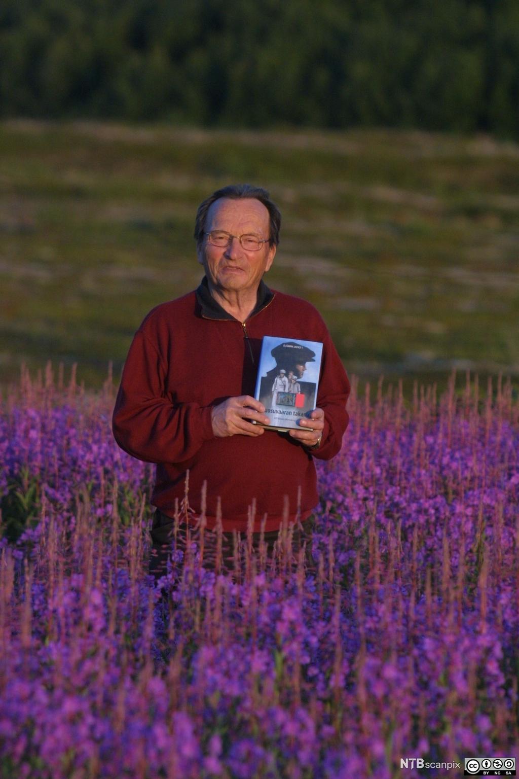 Forfatter Alf Nilsen-Børsskog i blomstereng med roman. Foto.
