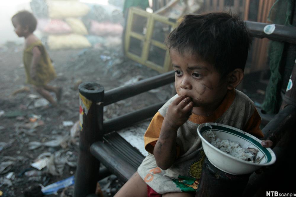 En fattigslig gutt spiser ris fra en bolle. Foto.