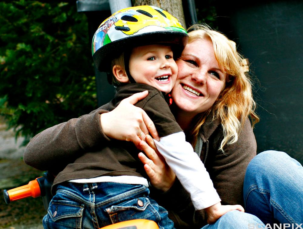 Kvinne klemmer en liten gutt med sykkelhjelm. Foto.
