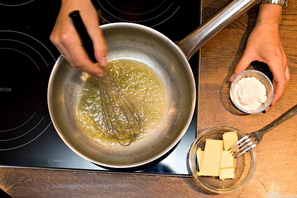 Ei hånd rører med visp i ei gryte med smeltet smør. To skåler, ei med hvetemel og ei med smør, står ved siden av. Foto.