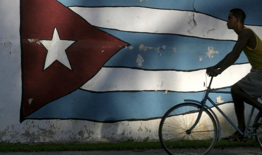 Ein mann syklar forbi det kubanske flagget i Havana. Foto.