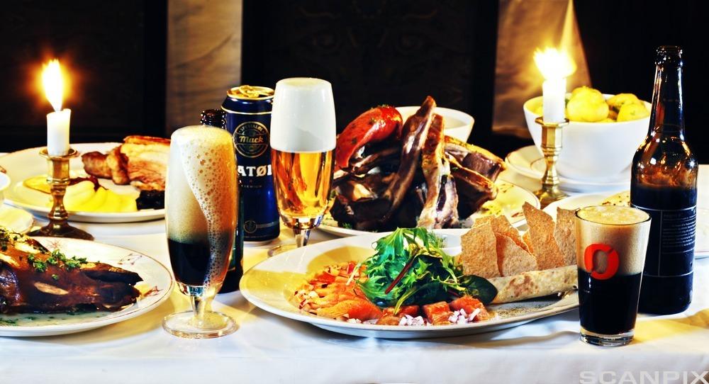 Tallerkener med julemat, ulike typer øl i glass og levende lys på et bord. Foto.
