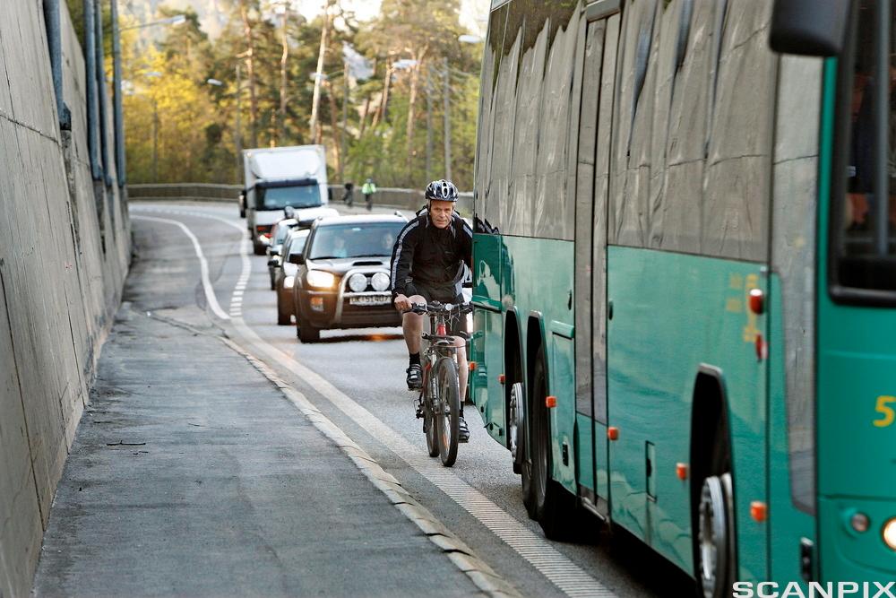 Person som sykler rett bak en buss. Foto.