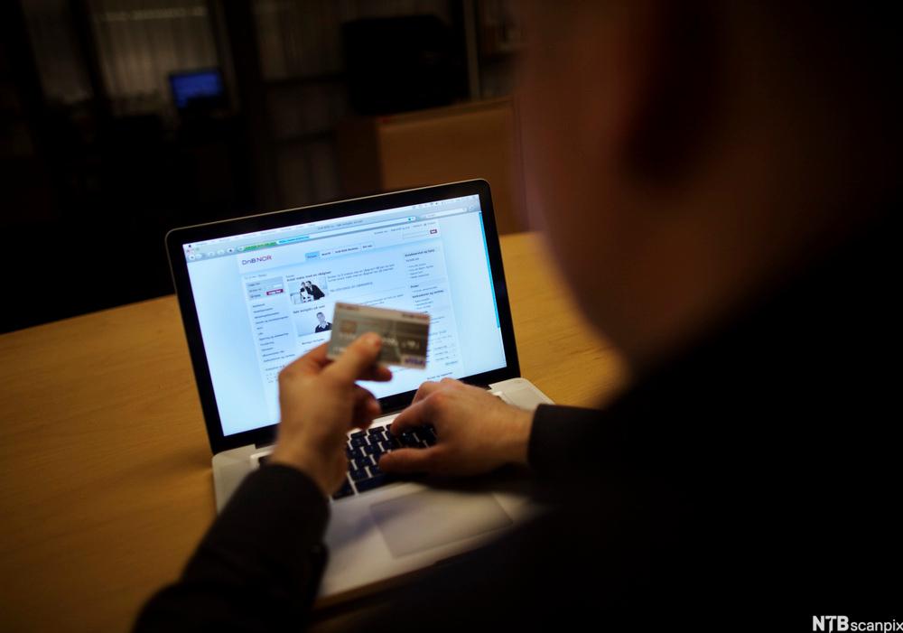 Person sitter foran bærbar datamaskin og legger inn informasjon fra bankkort. Foto.
