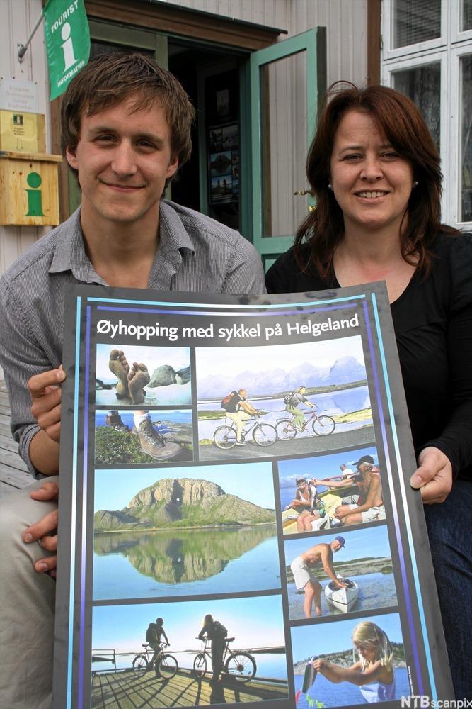 En mann og en kvinne sitter utenfor et turistkontor og viser fram en plakat med fine bilder av lokale turistopplevelser. Plakaten har overskriften "Øyhopping med sykkel på Helgeland". Foto.