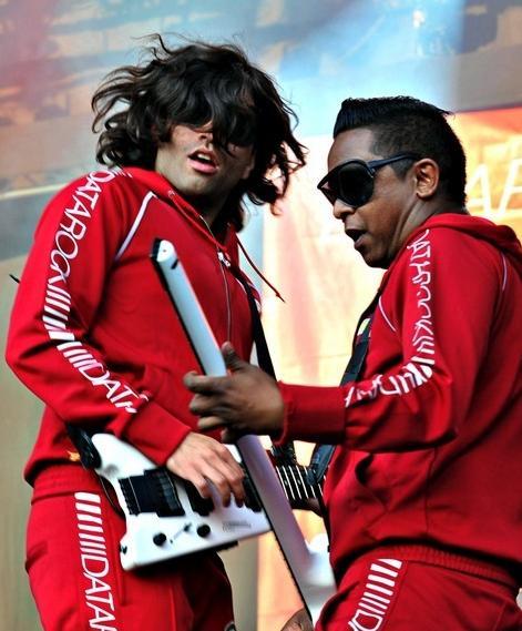 To menn i raud joggedress med teksten "DATAROCK" langs ermet. Dei har på seg store solbriller og speler på kvite gitarar på ei scene. Foto.